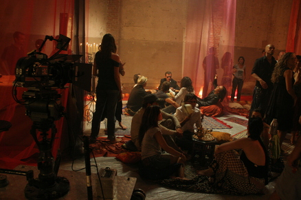 Grabadora filmando grupo de artista sentados en el suelo, rodeados de velas y alfombras.